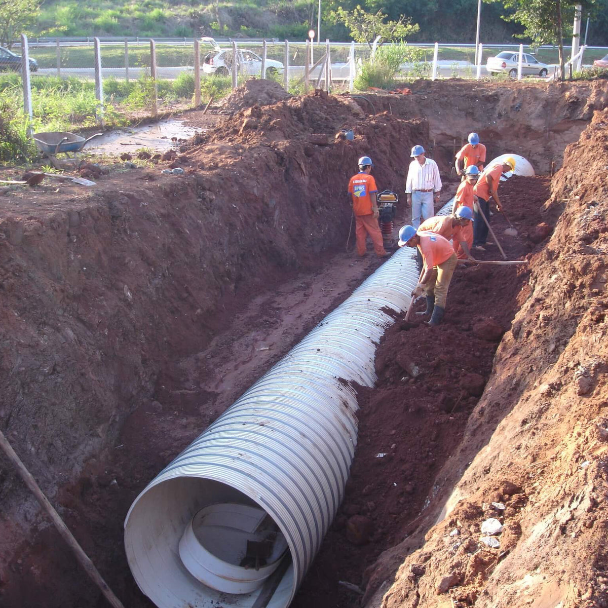 Tubo de PVC estruturado BR Loc assentado em vala de drenagem, com equipe compactando a envoltoria granular nas laterais