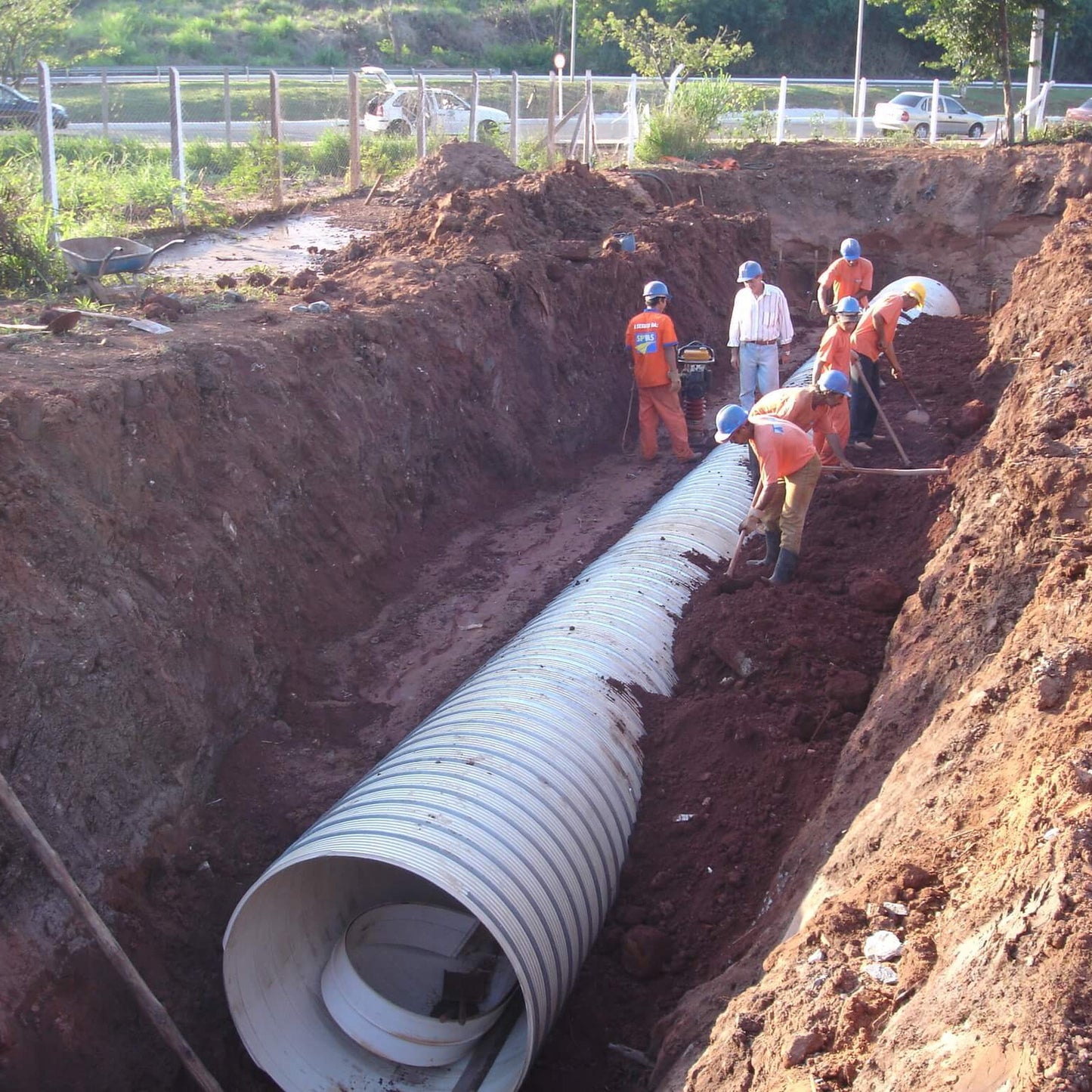 Tubo de PVC estruturado BR Loc assentado em vala de drenagem, com equipe compactando a envoltoria granular